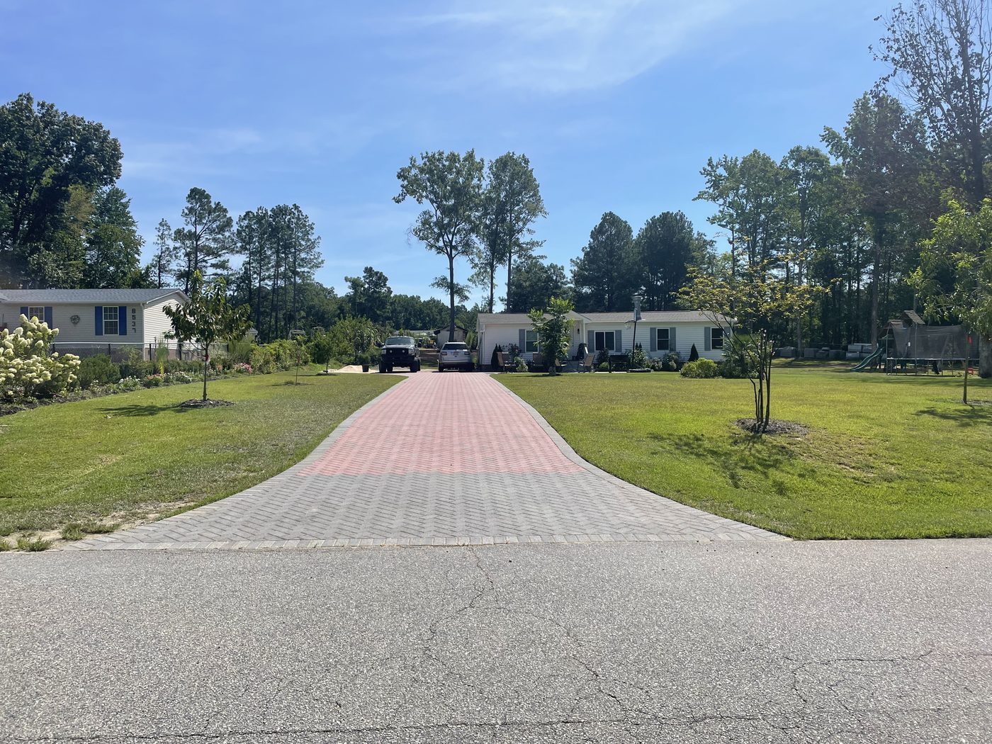 The finished brick paver driveway running from the street to the house, with grass grown in on both sides