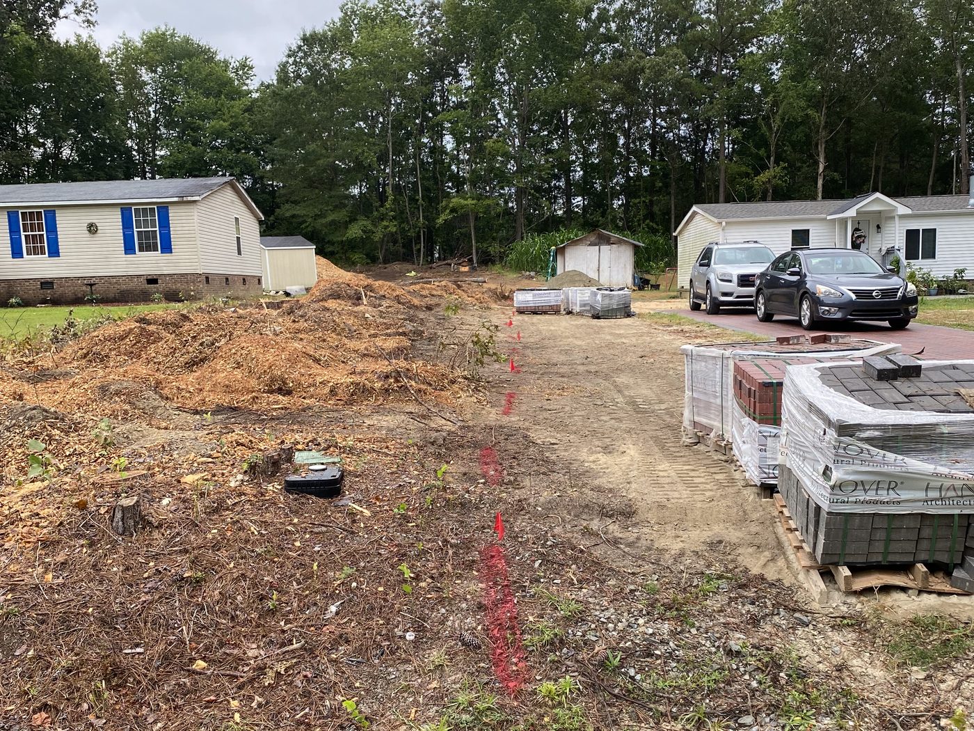 Bare dirt driveway marked with survey paint and stacked pallets of brick pavers before installation