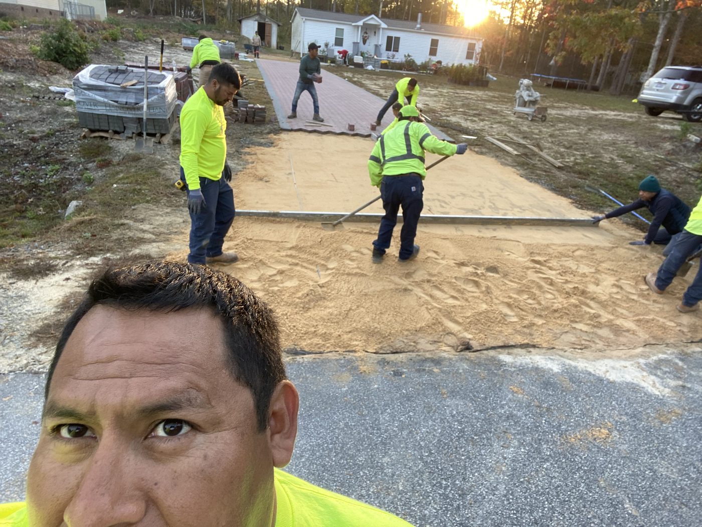 The Professional Landscape crew screeding the sand base and setting the first brick pavers on the driveway at sunrise