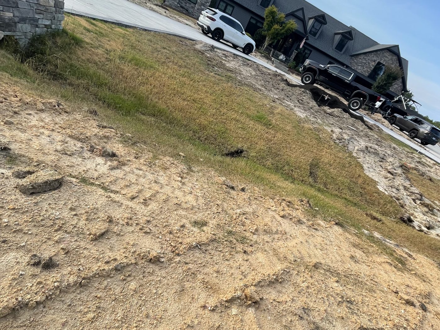 Bare, eroded dirt slope in front of a large stone and dark-sided house before landscaping