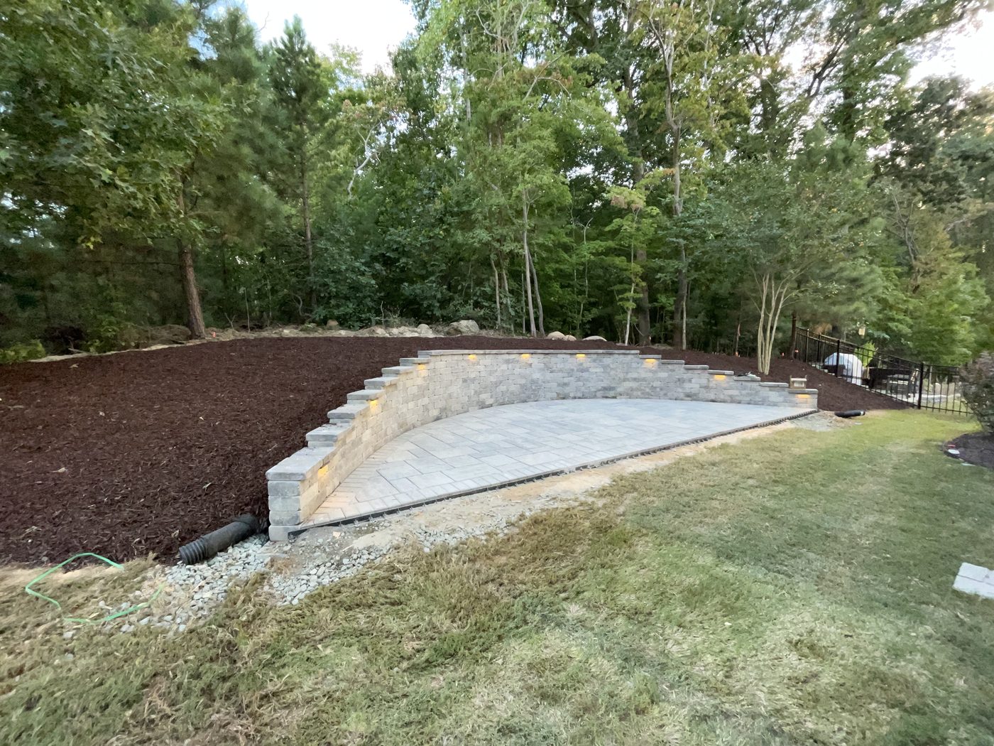 The same slope finished as a tiered stone terrace with lit steps and a paver patio