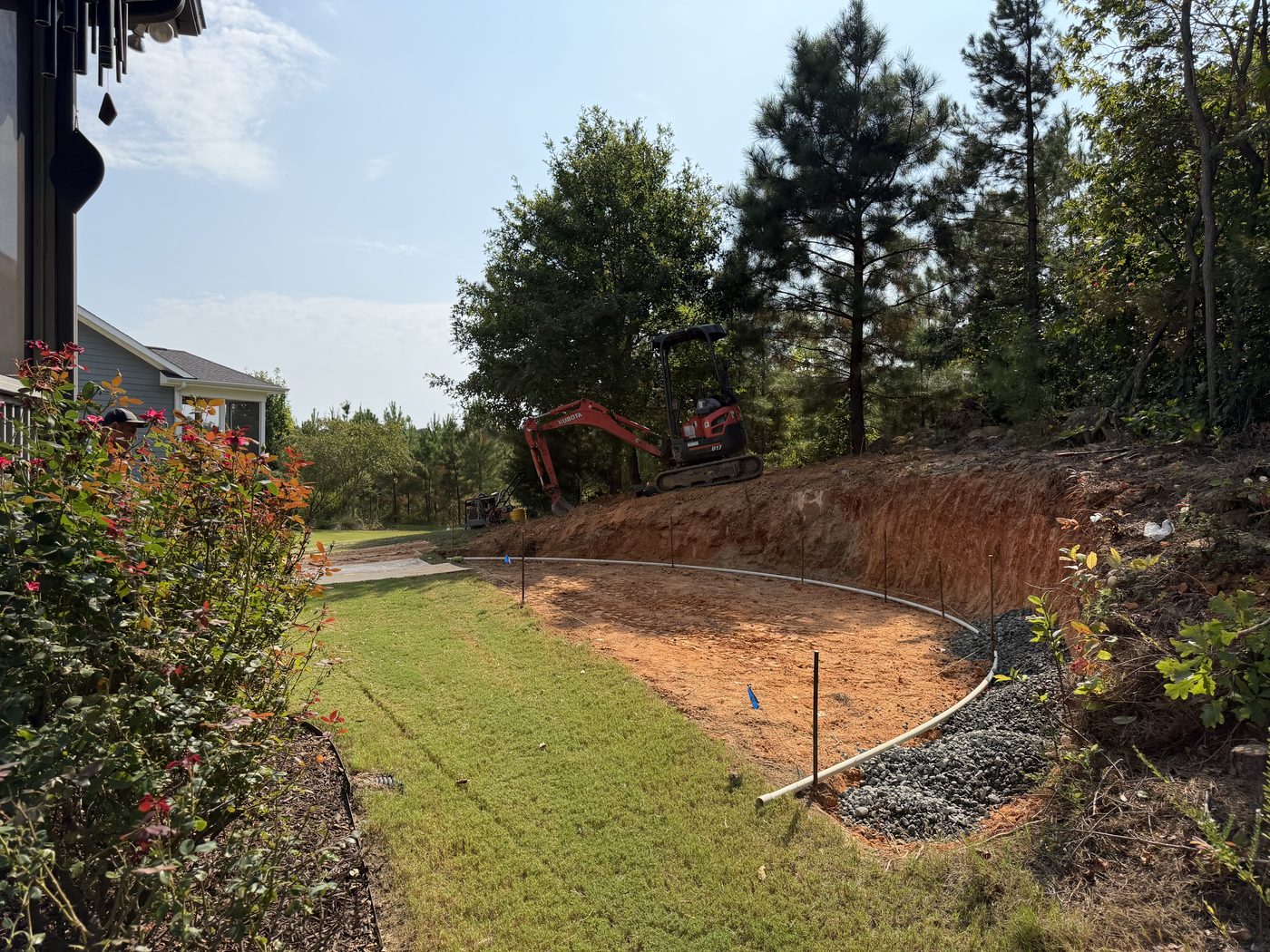 Excavated curved bank with gravel base and drainage pipe going in behind the new retaining wall