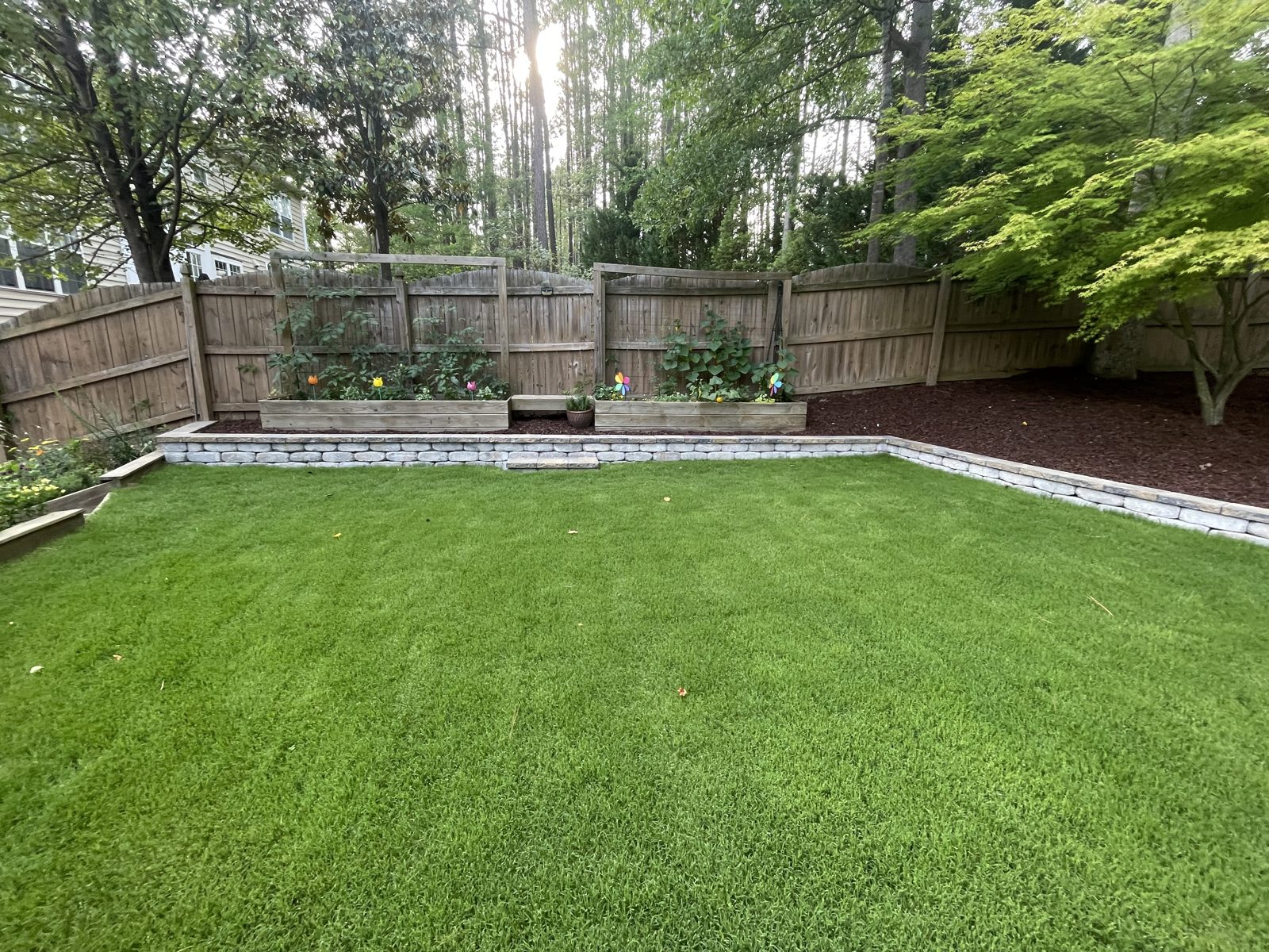 Backyard sod installation with a stacked stone retaining wall and raised planter beds